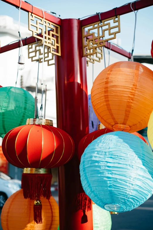 a bunch of colorful paper lanterns hanging from a pole, market setting, square, tall, center of image