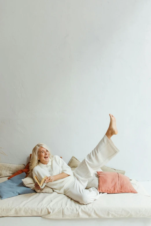 a woman laying on a bed reading a book, pexels contest winner, white hair floating in air, head bent back in laughter, in a white boho style studio, large)}]