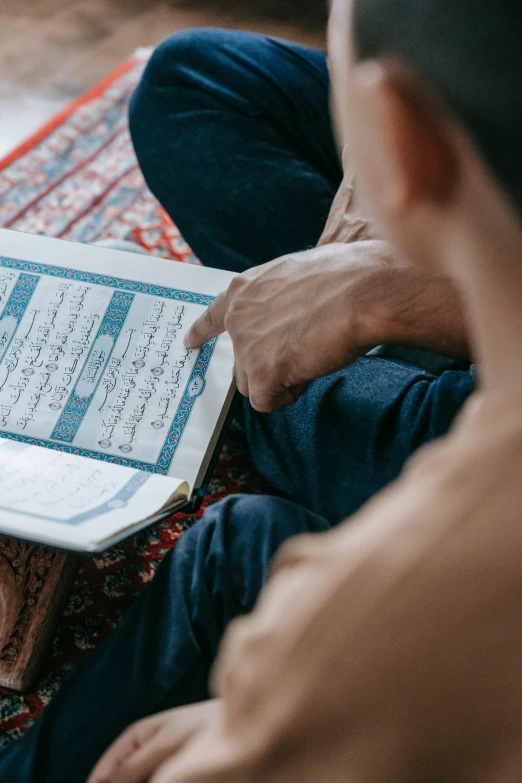 a man sitting on a rug reading a book, hurufiyya, fast paced, teaching, erak note, taken in 2 0 2 0