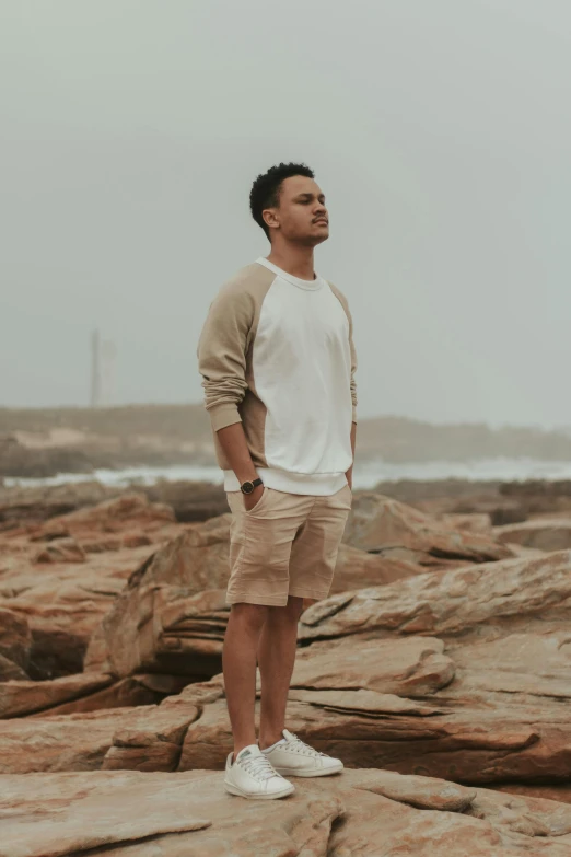 a man standing on top of a rocky beach, wearing a white sweater, tan skin a tee shirt and shorts, federation clothing, wearing a sweater