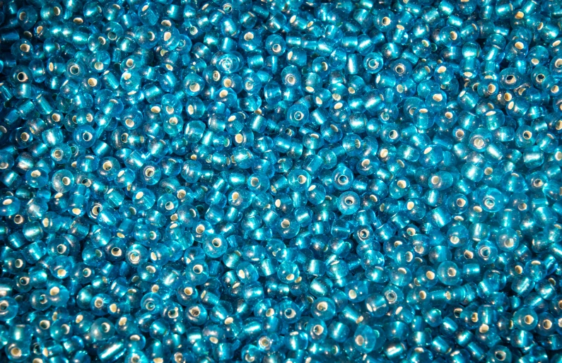 a pile of blue beads sitting on top of a table, dynamic pearlescent teal light, vibrant color with gold speckles, bird - eye view, rendered in arnold