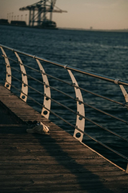 a close up of a railing near a body of water, inspired by Elsa Bleda, unsplash contest winner, warm lighting with cool shadows, calm seas, curved bridge, detailed shot legs-up