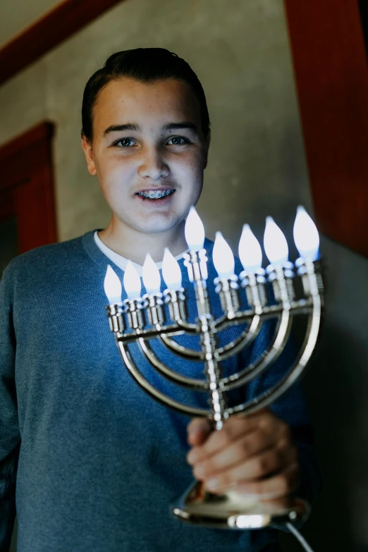 a boy holding a menorah with lit candles, 2019, around 1 9 years old, ap news photograph, ready to model