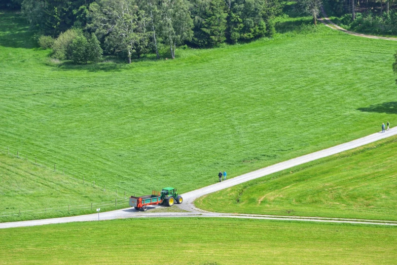 a tractor driving down a road next to a lush green field, by Andries Stock, pexels contest winner, les nabis, photo of zurich, people at work, sloped site, 🚿🗝📝