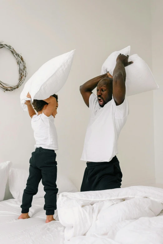 a couple of people standing on top of a bed, with a kid, white pillows, shaq, profile image