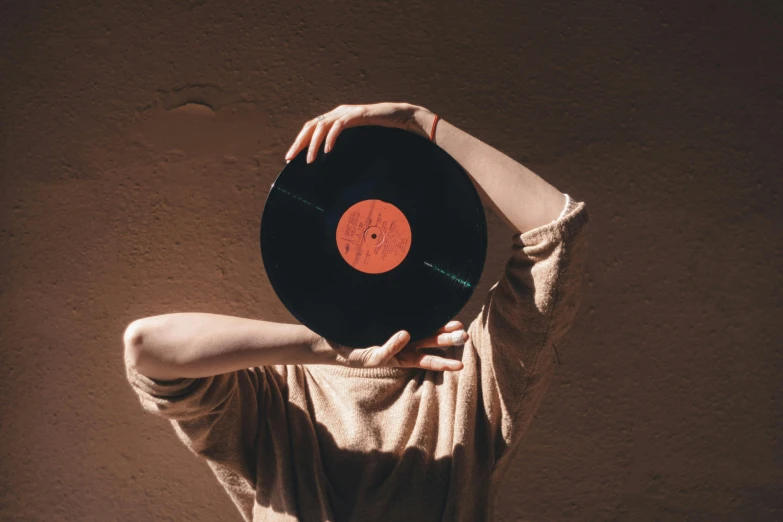 a woman holding a record in front of her face, by Romain brook, pexels contest winner, bauhaus, a round minimalist behind, greeting hand on head, an ancient, a wooden