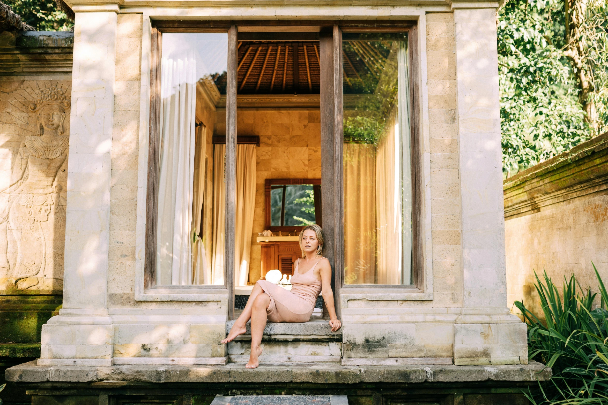 a woman sitting in a window of a building, lush surroundings, bali, kylie minogue, slightly golden