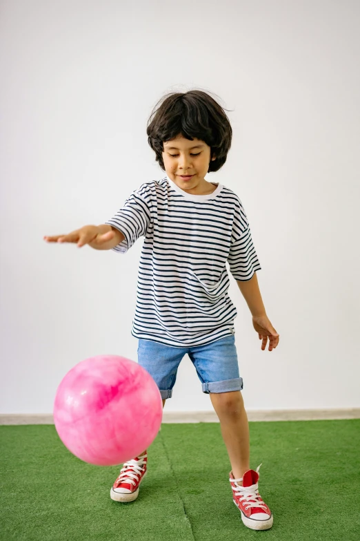 a young boy is playing with a pink ball, by Arabella Rankin, dribble contest winner, wearing stripe shirt, jaeyeon nam, inflatable, standing sideways