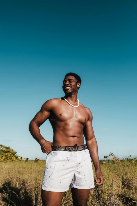 a man standing in the middle of a field, by Cosmo Alexander, trending on pexels, white skirt and barechest, bahamas, showing off his muscles, jaylen brown