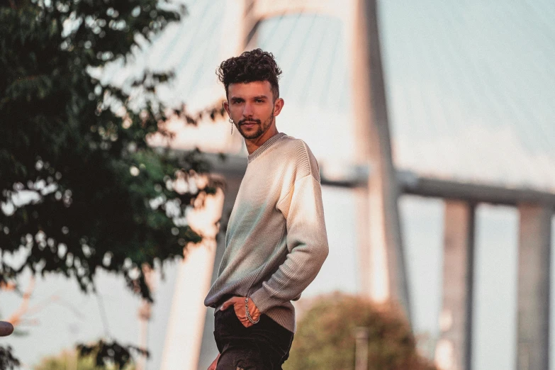 a man standing on a skateboard in front of a bridge, a picture, by Adam Marczyński, wearing a sweater, christian dimitrov, profile image, portrait image