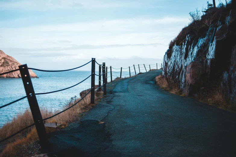 a road that is next to a body of water, unsplash, fence line, background image, cliff, high quality image”