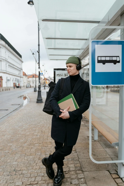 a man standing in front of a bus stop, headphones on head, reading, high-quality photo, non-binary