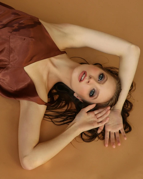 a woman in a brown dress laying on the ground, an album cover, inspired by Elizabeth Polunin, trending on pexels, renaissance, pale skin!, brown:-2, model face, high angle