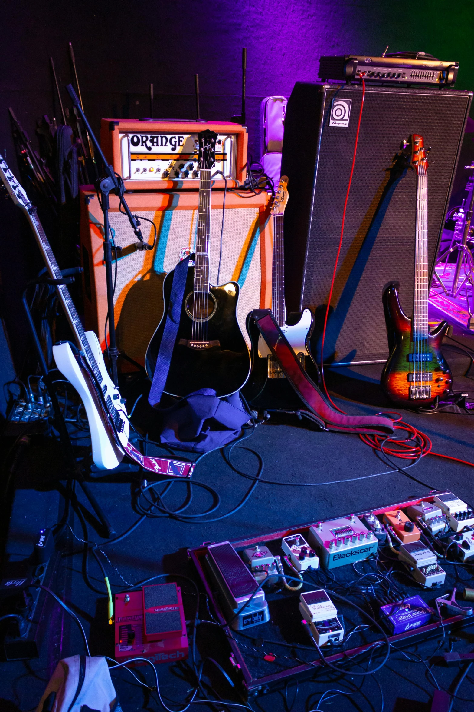 a group of guitars sitting on top of a stage, cable plugged into cyberdeck, purple scene lighting, wires and cords, the backroom
