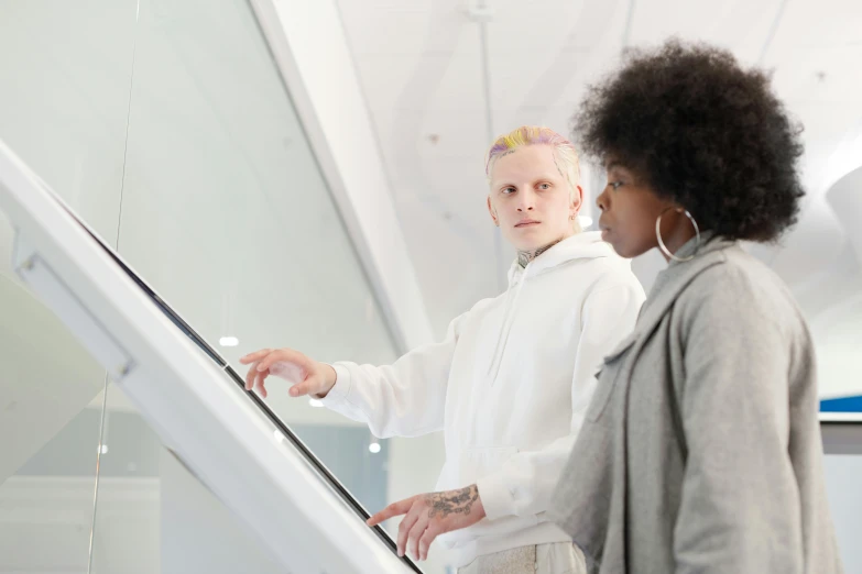 a couple of people standing next to each other on an escalator, trending on pexels, interactive art, albino hair, looking at monitor, whiteboards, muted colors. ue 5