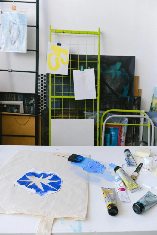 a white table topped with lots of art supplies, a silk screen, inspired by Yves Klein, behance, professional studio shot, stencil, yellow and blue, in a studio