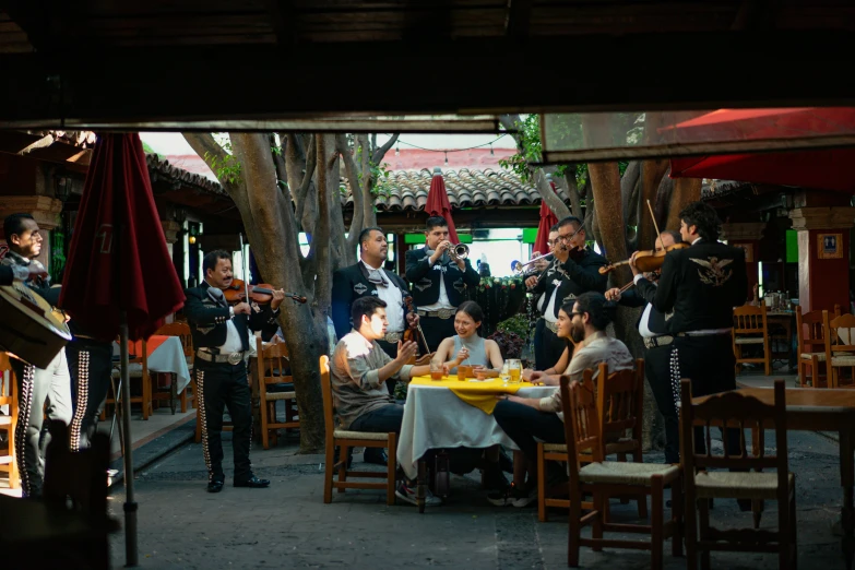 a group of people that are sitting around a table, by Alejandro Obregón, pexels contest winner, happening, tlaquepaque, orchestra, restaurant exterior photography, square