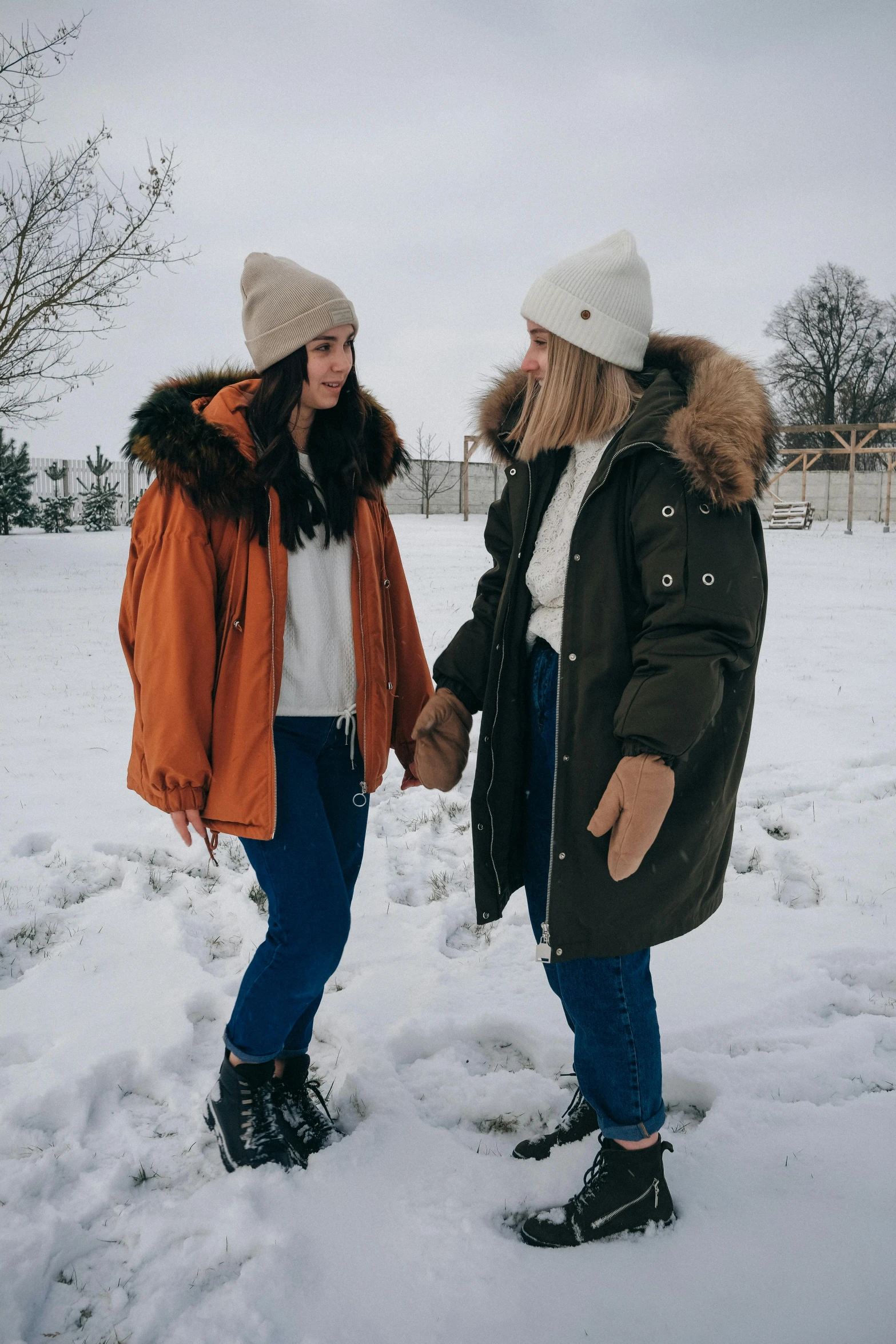 two women standing in the snow holding hands, a colorized photo, trending on pexels, beanie, brown tuffle coat, gif, gen z