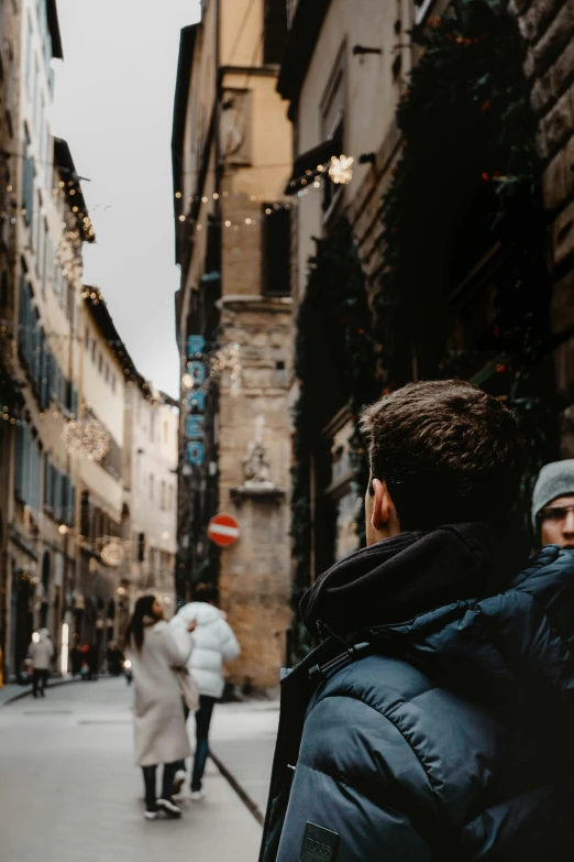 a man walking down a street next to tall buildings, a photo, by Alessandro Allori, renaissance, holiday season, two men hugging, bargello, portrait featured on unsplash