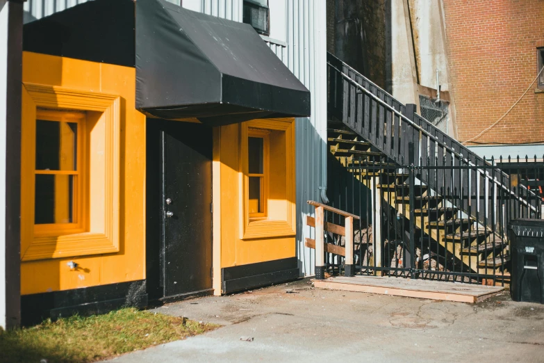 a black and yellow building with stairs in front of it, unsplash, private press, awnings, doorway, tilt and orange, thumbnail