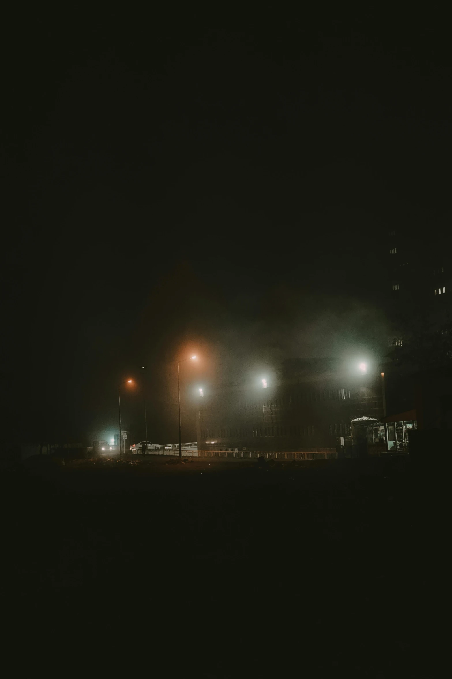 a couple of lights that are on in the dark, a picture, inspired by Elsa Bleda, fog fills the area, industrial fires and smog, moonlit parking lot, background ( dark _ smokiness )