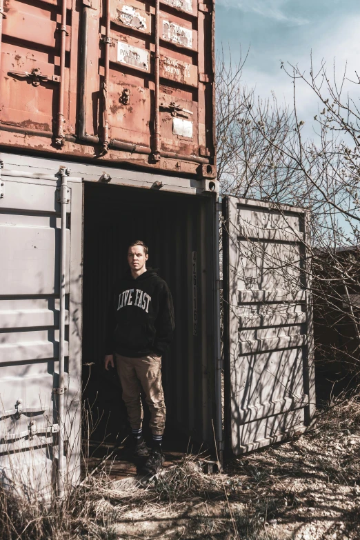 a man standing in the doorway of a shipping container, a portrait, pexels contest winner, trending on r/streetwear, full body picture, structure : kyle lambert, dylan cole