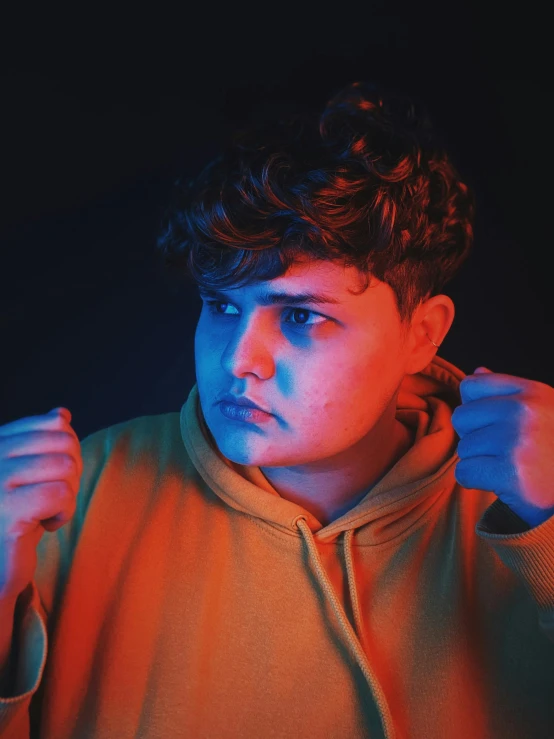 a young man standing in front of a black background, an album cover, inspired by Ion Andreescu, trending on pexels, overweight!! teenage boy, angry look, brightly colored, bisexual lighting