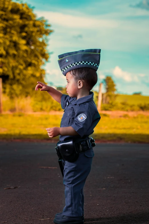 a little boy that is standing in the street, by Andrew Stevovich, pexels contest winner, happening, police cap, full costume, in a scenic background, te pae