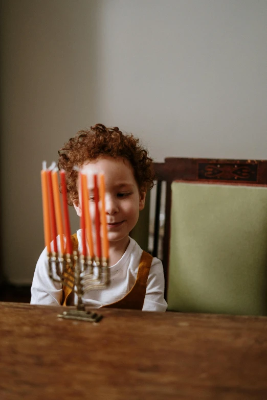 a little boy sitting at a table with a menorah, pexels, curly copper colored hair, holiday, diverse, instagram picture