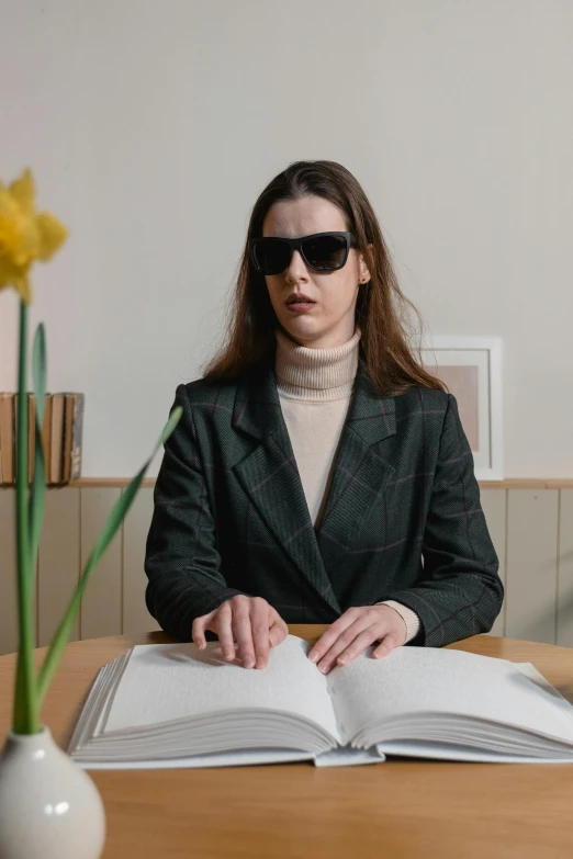 a woman sitting at a table with an open book, inspired by Elsa Bleda, wearing versace sunglasses, lawyer clothing, the non-binary deity of spring, wearing a turtleneck and jacket