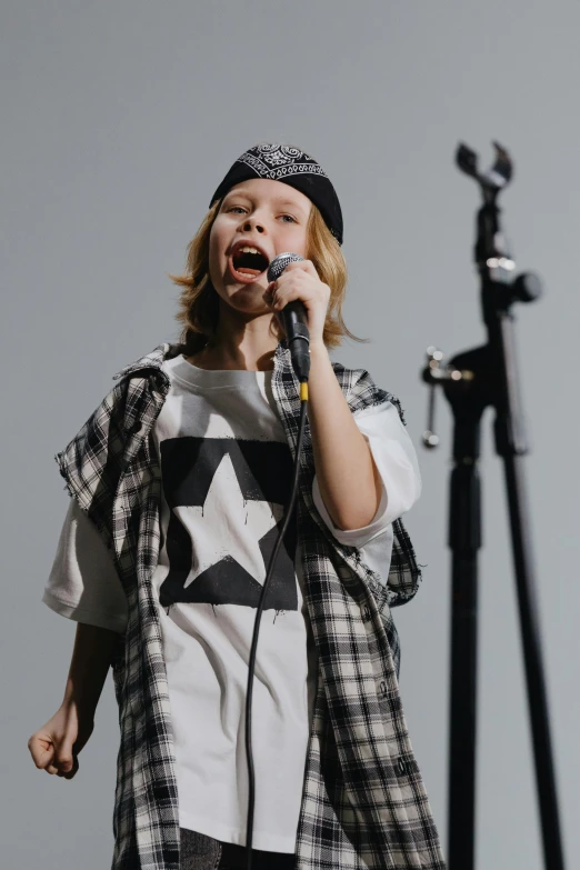 a woman singing into a microphone on a stage, trending on pexels, little boy, baggy clothing and hat, wearing punk clothing, modeling studio