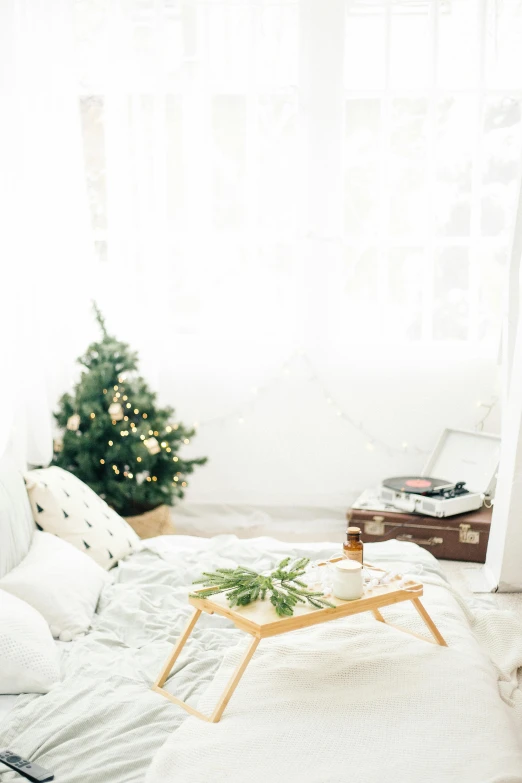 a white bed sitting under a window next to a christmas tree, an album cover, unsplash contest winner, light and space, in a white boho style studio, 4k), concert, snacks
