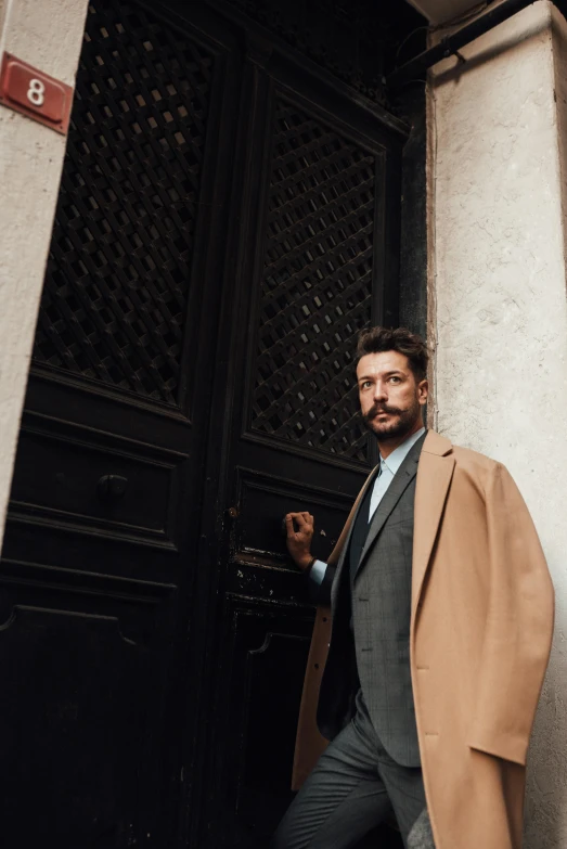 a man in a coat leaning against a building, by Carlo Martini, pexels contest winner, renaissance, shia labeouf, exiting from a wardrobe, guido reni style, subject detail: wearing a suit