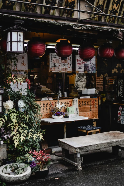 a man sitting on a bench in front of a store, inspired by Takeuchi Seihō, trending on unsplash, mingei, tea drinking and paper lanterns, archways made of lush greenery, food stall, street view