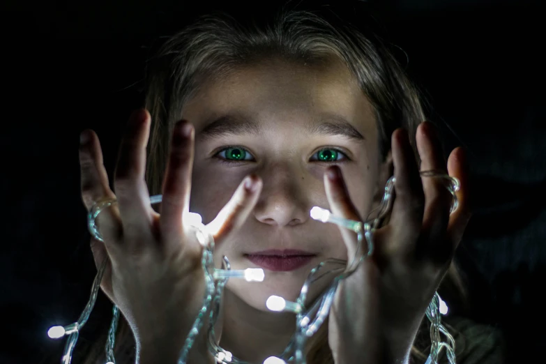 a close up of a person holding a string of lights, by Adam Marczyński, pexels contest winner, hyperrealism, teenage girl, sci fi, family photo, hands on face