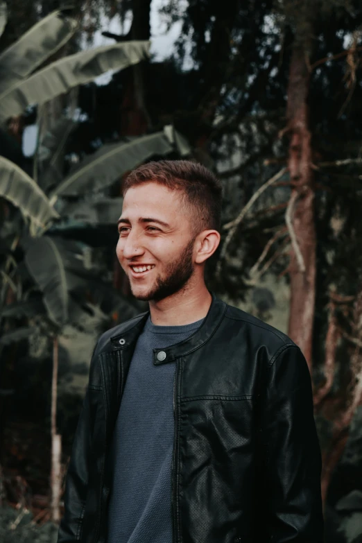 a man standing in front of a banana tree, an album cover, pexels contest winner, headshot profile picture, gal yosef, wearing leather jacket, smiling sweetly