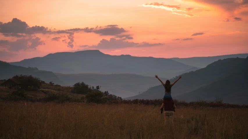 a woman standing in a field with her arms in the air, by Daniel Lieske, pexels contest winner, sunset in a valley, african plains, pink, hills in the background