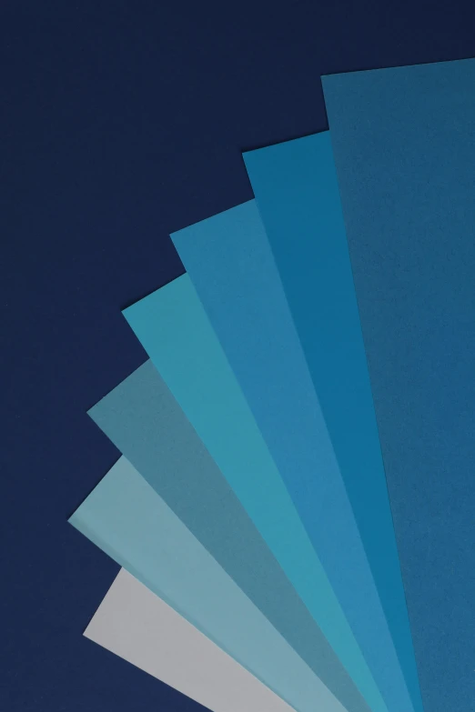 a stack of blue sheets of paper against a dark blue background, spectrum colours, various sizes, shoreline, cardstock