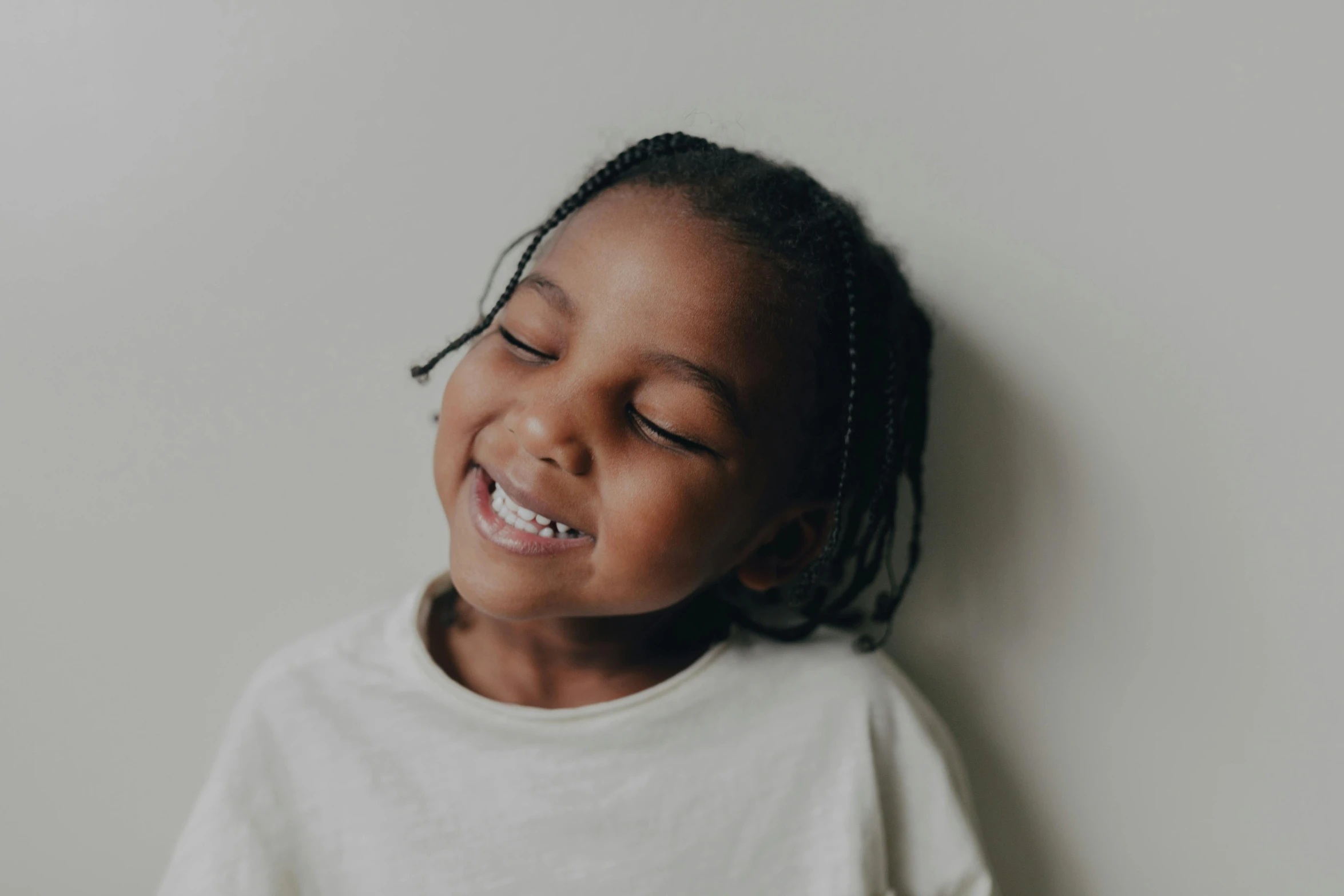 a little girl smiling with her eyes closed, pexels contest winner, young black woman, plain background, leaning against the wall, with a white complexion