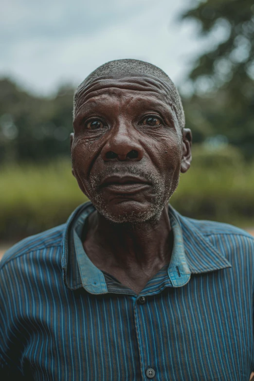 a man in a blue shirt holding a banana, by Will Ellis, pexels contest winner, wrinkly forehead, african man, portrait of forest gog, in the center of the image