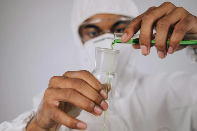 a man in a lab coat pouring green liquid into a beaker, an album cover, trending on pexels, muslim, ski mask, engineering, white