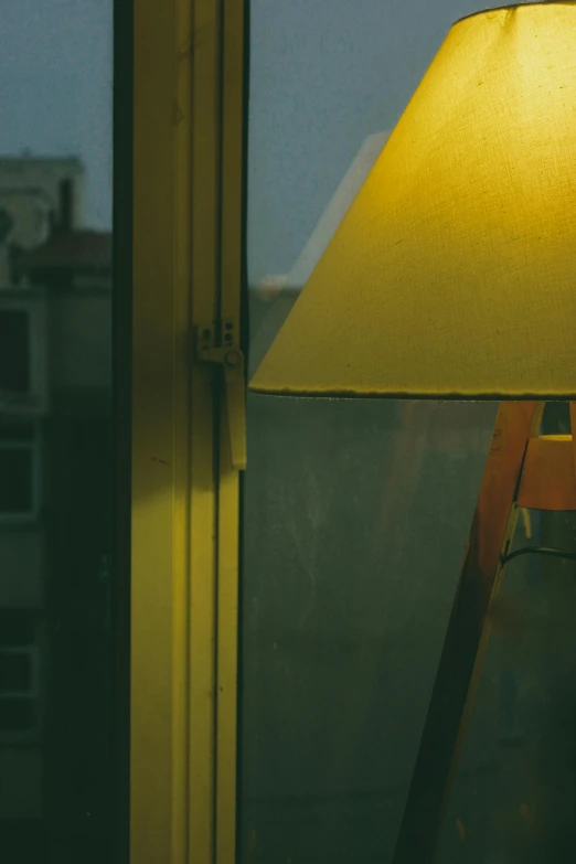 a lamp sitting on top of a table next to a window, inspired by Elsa Bleda, realism, yellow, zoomed in, medium-shot, window ( city )