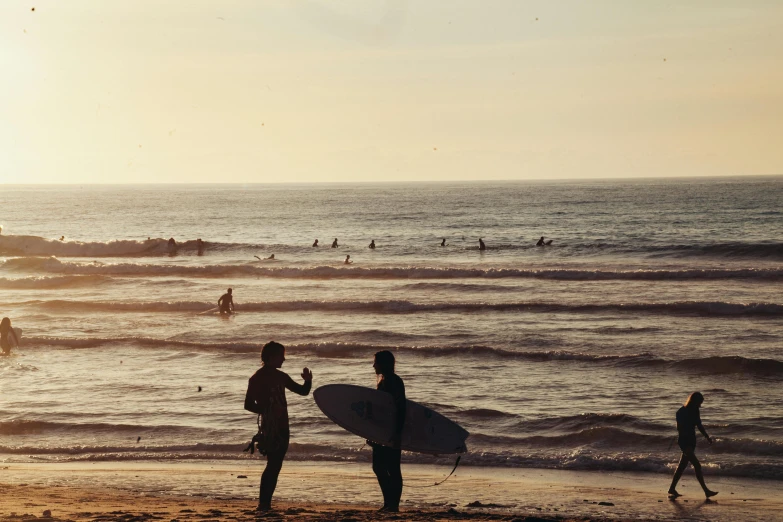 a group of people standing on top of a beach next to the ocean, surfing, profile image