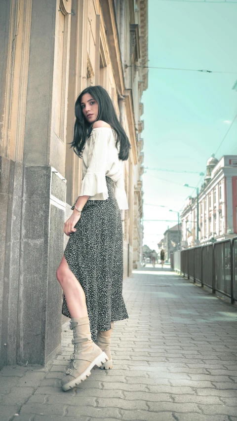 a woman standing on a sidewalk next to a building, by Andries Stock, pexels contest winner, renaissance, female with long black hair, bohemian fashion, long skirt, promotional image