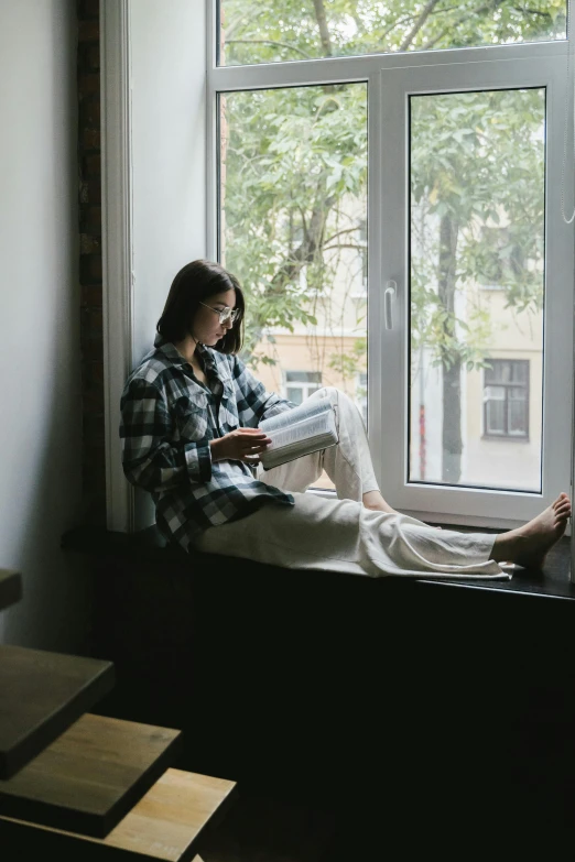 a woman sitting on a window sill reading a book, extremely uncomfortable, 2019 trending photo, in a room, studious