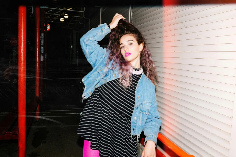 a woman that is standing in front of a wall, an album cover, inspired by Elsa Bleda, trending on pexels, happening, curly pink hair, purple and black clothes, wearing stripe shirt, harsh flash photo at night