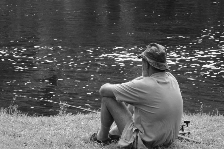 a man sitting on the grass next to a body of water, a picture, inspired by Louis Faurer, pixabay contest winner, precisionism, fishing, monochrome:-2, shaded, waiting to strike