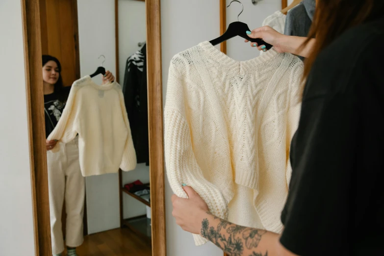 a woman standing in front of a mirror holding a sweater, trending on pexels, wearing a white sweater, inspect in inventory image, witch clothes, wearing casual sweater