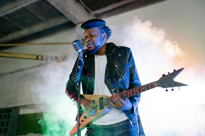 a man holding a guitar and singing into a microphone, unsplash, happening, industrial party, ( ( dark skin ) ), skies behind, coloured