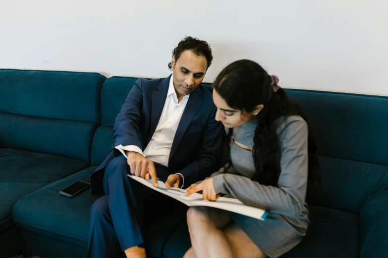 a man and a woman sitting on a blue couch, by Gavin Hamilton, pexels contest winner, hurufiyya, wearing business casual dress, with notes, middle eastern, on a white table